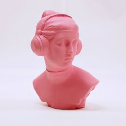 A pink, abstract statue of a female figure with a stylized, geometric hairstyle. The statue has a modern, minimalist design and appears to be made of a smooth, glossy material.