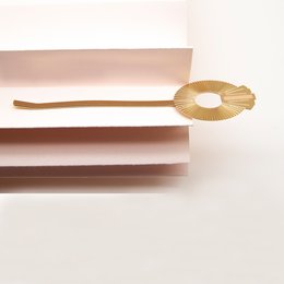 A gold-colored hair clip with a round, floral-shaped design and a long, thin stem. Available in a variety of neutral and earthy color variants including blanc, nude, mousse, noir, ambre, brique, midnight blue, prusse, corail, aniline, sable, and massaï.